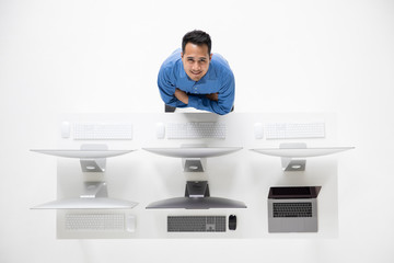 Young Asian businessman standing and look up to camera at high angle beside group of new computers.