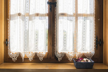 A Wooden Window With A White Embroidered Curtain And A Small Basket Of Dried Flowers On The Windowsill