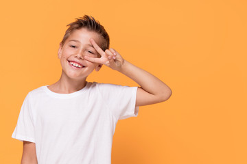 Young emotional little boy on orange studio background.