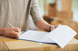 © DragonImages - Crop view of male hands putting signature to document in clipboard placed on packed delivered carton box on blurred background