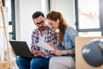 Young couple moving in new home. Sitting and relaxing after unpacking. Searching home decorating ideas on laptop