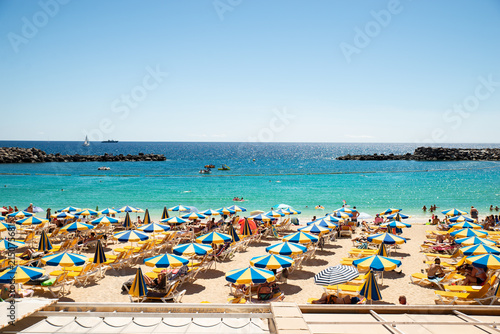 Fotografia, Obraz Las Americas, Canarias islands/ Spain-July 22, 2018: View of beach fool of tourists and umbrellas for sun on Canarias, view of bay with mountains