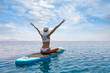 canvas print picture - Frau in weißem Bikini und mit Sonnenhut genießt ihren Urlaub auf einem Surfbrett über blauem, sommerlichen Meer