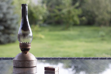 The old antique kerosene  oil lamp  with smoked glass on table in front of bokeh blurred garden. Place for text. Nostalgic scene.