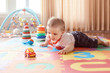 © anoushkatoronto - Portrait of cute adorable blond Caucasian smiling child boy with blue eyes crawling on floor in kids children room. Little baby playing with toys on playmat at home. Early education development