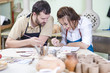 © danmorgan12 - Two Professional Ceramists Glazing and Painting Ceramic Clay Tiles in Workshop Together.Group of Cups on Foreground.