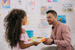 © LIGHTFIELD STUDIOS - african american preschooler giving picture to smiling caucasian teacher in classroom