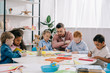 © LIGHTFIELD STUDIOS - teacher and interracial preschoolers at table with paints and papers in classroom
