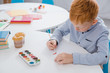 © LIGHTFIELD STUDIOS - focused preschooler red hair boy drawing picture at table in classroom