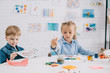 © LIGHTFIELD STUDIOS - focused preschoolers drawing pictures with paints and paint brushes at table in classroom