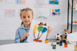 © LIGHTFIELD STUDIOS - portrait of little kid showing colorful picture in hands while sitting at table in room