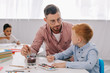 © LIGHTFIELD STUDIOS - teacher helping little boy to draw picture at table in classroom
