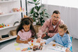 © LIGHTFIELD STUDIOS - teacher in eyeglasses and multiracial children drawing pictures with paints at table in classroom