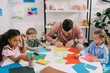 © LIGHTFIELD STUDIOS - multiethnic preschoolers and teacher making paper applique at table in classroom