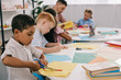 © LIGHTFIELD STUDIOS - selective focus of teacher and interracial preschoolers cutting colorful papers with scissors in classroom