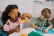 © LIGHTFIELD STUDIOS - portrait of multicultural classmates sitting at table with papers in classroom