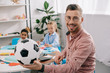 © LIGHTFIELD STUDIOS - smiling teacher with soccer ball and multicultural classmates behind in classroom
