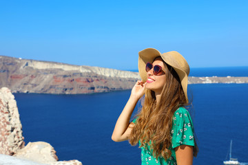 Wall Mural - Beautiful young woman with hat and sunglasses enjoying the sun in Santorini with the Caldera on background, Greece, Europe