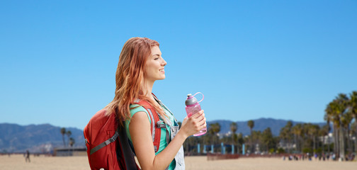 Wall Mural - adventure, travel, tourism, hike and people concept - smiling young woman with backpack and bottle of water over venice beach background in california