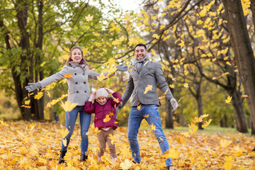 Wall Mural - family, season and people concept - happy mother, father and little daughter playing with autumn leaves at park