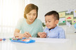 © DragonImages - Young woman teacher and cute Asian boy drawing with crayons in art class in backlit