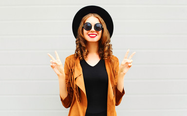 Cool girl wearing a black hat, sunglasses and jacket over urban grey background