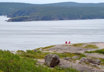 high angle view towards two empty red Adirondack chairs on the edge of a cliff overlooking the ocean, Signal Hill St John's Newfoundland Canada