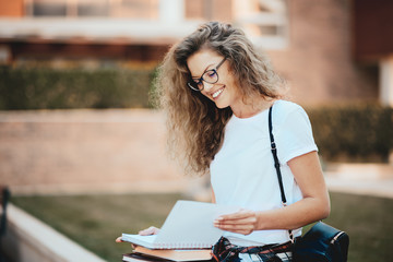 Female student sitting on bench and reading book.