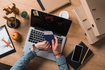 cropped shot of businessman holding flight ticket and looking at wrist watch at workplace