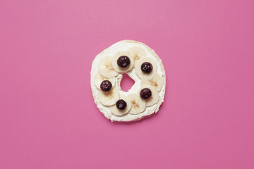 Blueberry and banana bagel with cream cheese on a pastel pink background