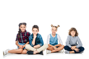 Wall Mural - four schoolchildren sitting and looking at camera isolated on white