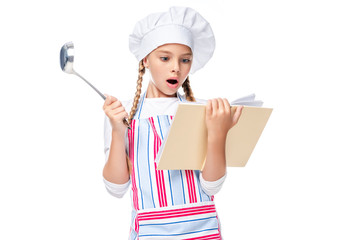 Wall Mural - shocked schoolchild in costume of chef reading cookbook isolated on white