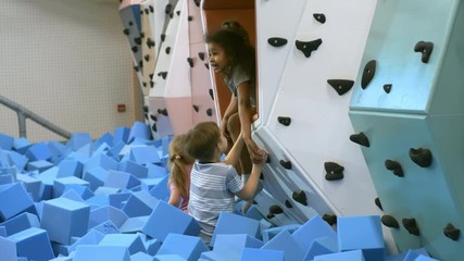 Wall Mural - Tilt down shot of two little girls not letting friends use indoor climbing wall in children play center