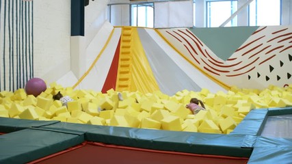 Wall Mural - Group of four multi ethnic children jumping into cube pit with yellow soft foam cubes when spending time in indoor playground
