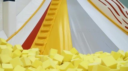 Wall Mural - Tilt down shot of four carefree children of diverse ethnicities sliding down into cube pit when playing in indoor amusement park