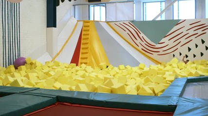 Wall Mural - Tilt down shot of multi ethnic group of children sitting with hands in the air on top of inflatable structure and sliding down together into cube pit when having fun in indoor playground