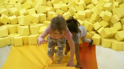 Wall Mural - Top view of three adorable children of different ethnicities climbing stairs of inflatable structure when having fun together in cube pit