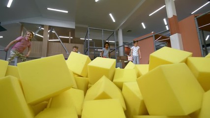 Wall Mural - Front view of four multi ethnic children jumping towards camera into cube pit with yellow soft foam cubes
