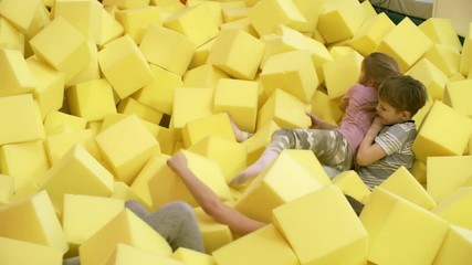 Wall Mural - Adorable children of elementary school age having play fight with yellow soft foam cubes in cube pit