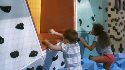 Wall Mural - Two multi ethnic children, boy and girl, playing on climbing wall with cube pit when spending time in indoor amusement park