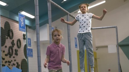 Wall Mural - Handheld shot of two cute girls jumping and bouncing on indoor trampoline together when spending time in children play center