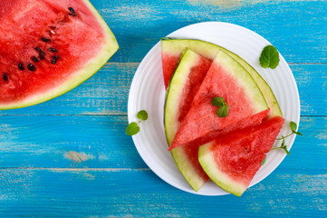 Wall Mural - Ripe juicy red watermelon slices on a white plate on a blue wooden background. Top view.