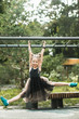 © Ira Efremova Photography/Stocksy - Cute little girl in a dark gray dress hanging from the jungle gym