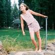 © Carleton Photography/Stocksy - Ten year old girl in stars and stripes romper at a cabin on a windy day