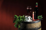 Fototapeta  - Butelka czerwonego wina i kawa w świetle świecy na beczce z winogronem.