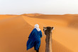 © Bisual Studio/Stocksy - Rear view of Berber and camel walking through dunes