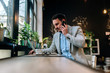 © bnenin - Modern businessman talking on a smartphone while working on laptop in the cafe.