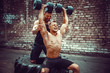 © zamuruev - Two muscular athletes training, one raise, push the barbbell when other is motivating. Scream. Working hard. Street gym. Exercise for the shoulder muscles, deltoid.
