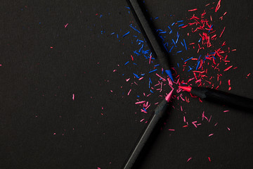 Black, colored pencils, on black background, and shavings from the pencils