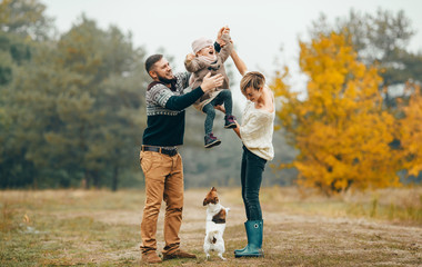 Happy parents have fun with their daughter at forest path next to dog during walk.